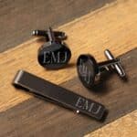 Engraved gunmetal tie bar and cufflinks against a wood background