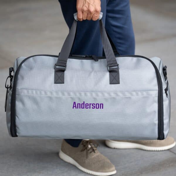 Grey suit saver bag with purple personalization thread being held by the carrying handles
