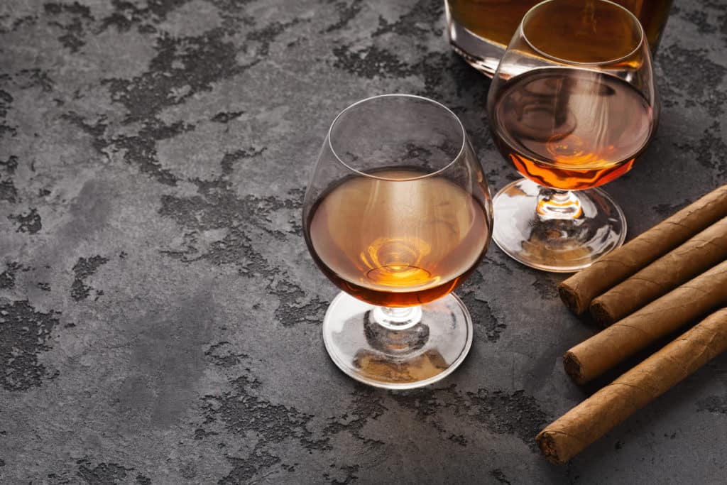 Luxe lifestyle attributen van groomsmen. Twee glazen met cognac en sigaren op marmeren tafel, kopieerruimte