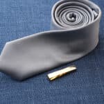 A gold tie clip being paired with a gray tie
