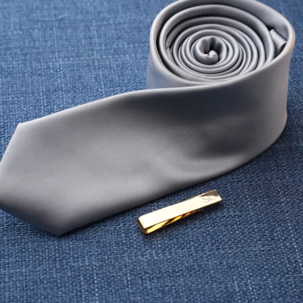 A gold tie clip being paired with a gray tie