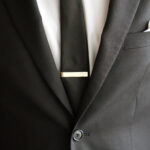 A groom wearing a gold tie bar with a black wedding suit
