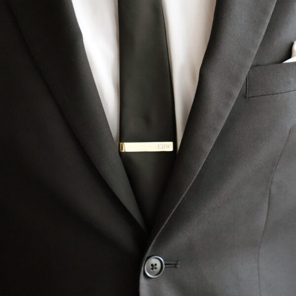 A groom wearing a gold tie bar with a black wedding suit