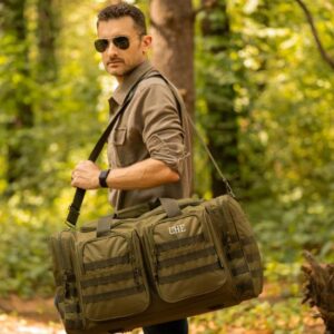A man carrying a military-style green duffle bag in the woods.