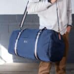 A man holding the monogrammed navy blue nylon duffle bag over his shoulder