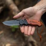 A man holding the wood pocket knife in a rustic forest setting