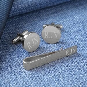 Silver cuff links and tie bar against a blue background