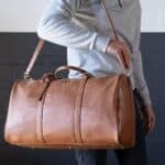 A man using the shoulder strap to hold his brown vegan leather embroidered duffle bag