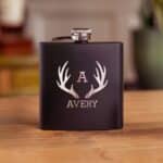 Black matte metal groomsmen flask shown with customer antler monogram