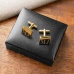 Engraved gold square cufflinks sitting on black storage box