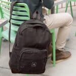 A student sitting outdoors while his black custom backpack rests by his side