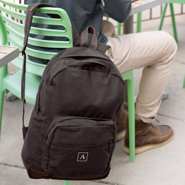A student sitting outdoors while his black custom backpack rests by his side