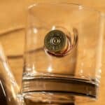 Close-up of the Federal Premium® 12 gauge shotgun shell casing that's embedded in the side of the whiskey glass
