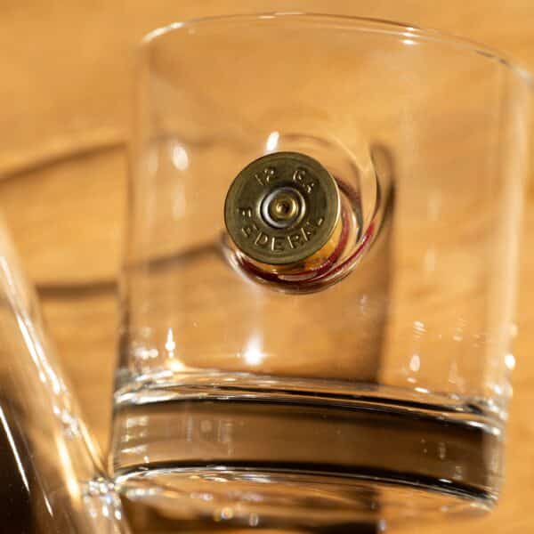 Close-up of the Federal Premium® 12 gauge shotgun shell casing that's embedded in the side of the whiskey glass