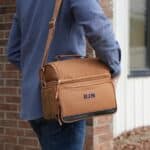 The brown lunch cooler being worn over a shoulder using the adjustable (and removable) strap