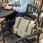 Man sitting on an outside table with his khaki laptop bag resting beside him on a chair