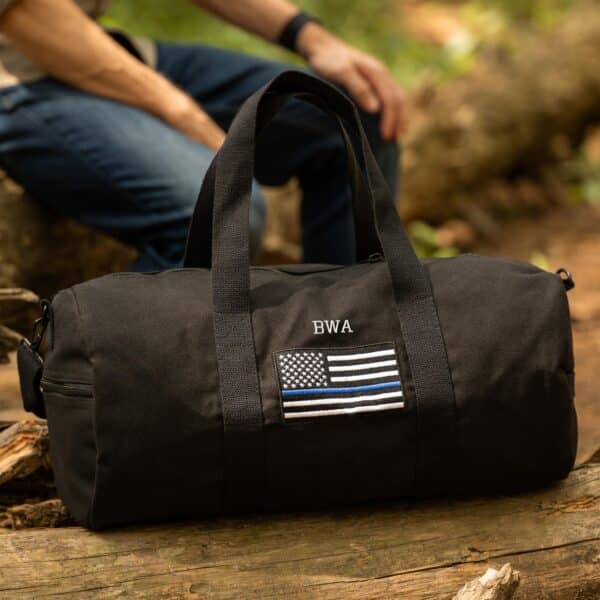 Man sitting in the woods with a black custom tactical duffle bag