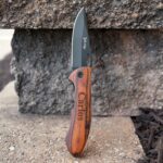 Elk Ridge Trail Knife with blade open, sitting vertically against a stone wall