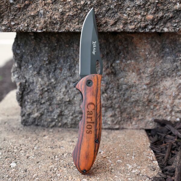 Elk Ridge Trail Knife with blade open, sitting vertically against a stone wall